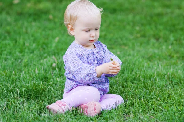 Söt rolig baby flicka sitter på gräset på en äng — Stockfoto