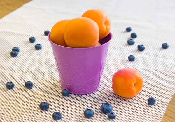 Albaricoques en un cubo violeta y arándanos sobre un fondo blanco —  Fotos de Stock