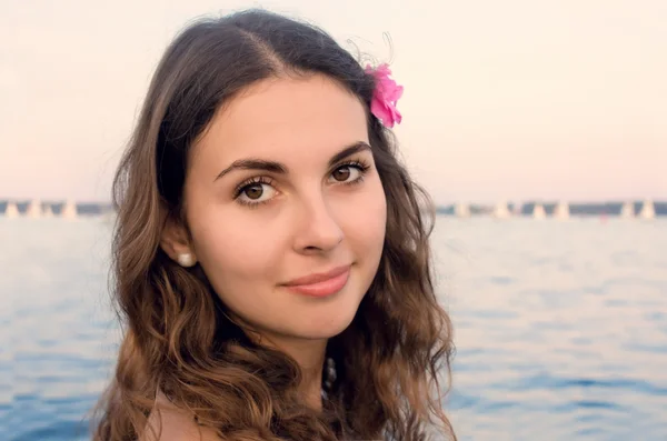 Chica con flor rosa por el agua — Foto de Stock