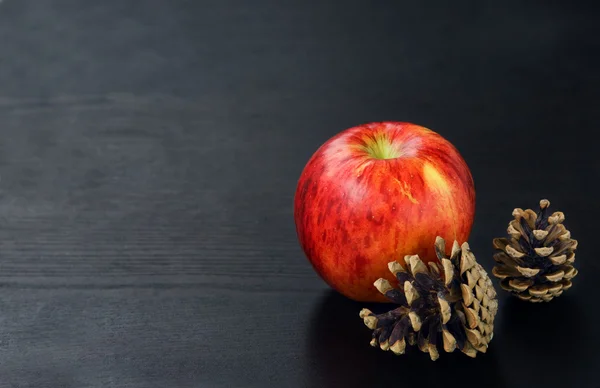 Denneappels en apple op zwarte houten achtergrond — Stockfoto