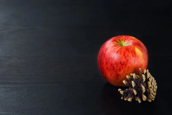 Cono de pino, manzana sobre fondo de madera negro —  Fotos de Stock