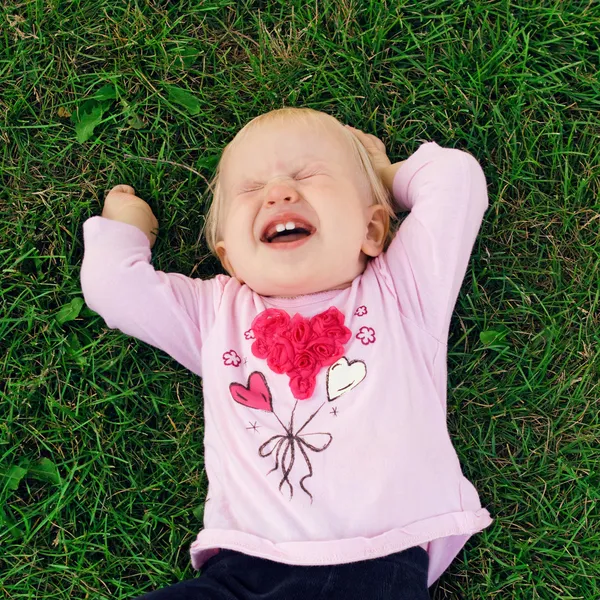 Roztomilý smějící se holčička na trávě — Stock fotografie