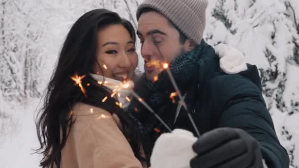 Liebespaar im Schneewald küsst und hält Wunderkerzen. Paar in der Winternatur. Paar feiert — Stockvideo