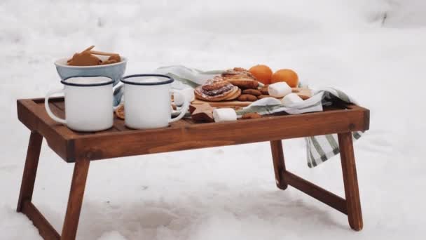 Çay fincanları, marşmelovlar, portakallar, kurabiyeler olan kış pikniği masası. Kardaki Noel Masası — Stok video