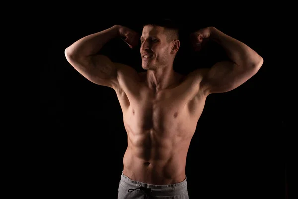 Ο άνθρωπος που δείχνει Biceps χέρια επάνω. Αθλητής που δείχνει μύες. ABS, δικέφαλοι μύες. Μαύρο φόντο. τόπλες άνθρωπος κοιτάζοντας προς τα πλάγια — Φωτογραφία Αρχείου