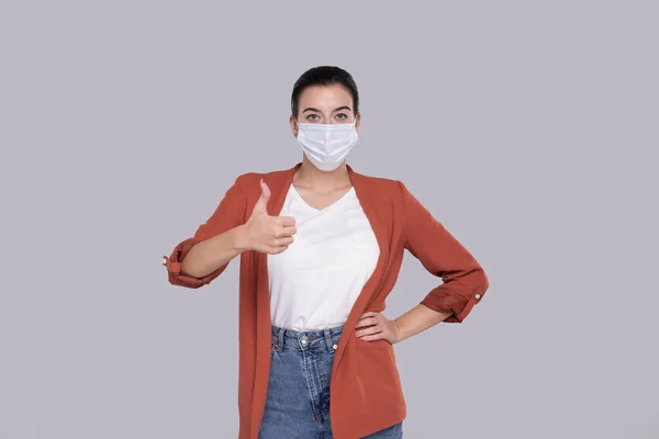 Девушка в медицинской маске, показывающая, что большой палец изолирован. Здравоохранение, медицина, образование — стоковое фото