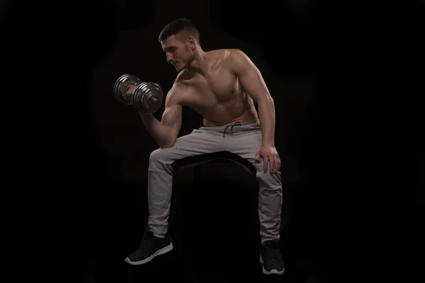 Ο άνθρωπος που κάθεται χτυπώντας Biceps με Dumbbell στο μαύρο δωμάτιο. Ο Σπρότσμαν κάνει τρανσέξουαλ στους δικέφαλους μυς. Γυμναστήριο, Lifting Sport Concept. — Φωτογραφία Αρχείου