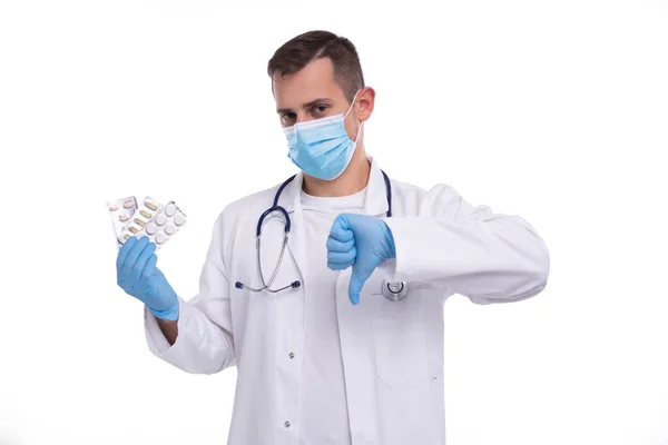 Hombre Doctor mostrando píldoras y pulgar hacia abajo usando máscara médica y guantes. Doctor sosteniendo tabletas. Hombre Doctor aislado. —  Fotos de Stock