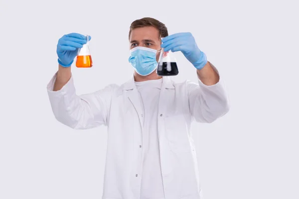 Masculino Doctor Examing Flask com Colorfull líquido vestindo máscara médica, luvas isoladas. Ciência, Medicina, Conceito de Vírus. Homem Doutor Smilling. Líquido — Fotografia de Stock