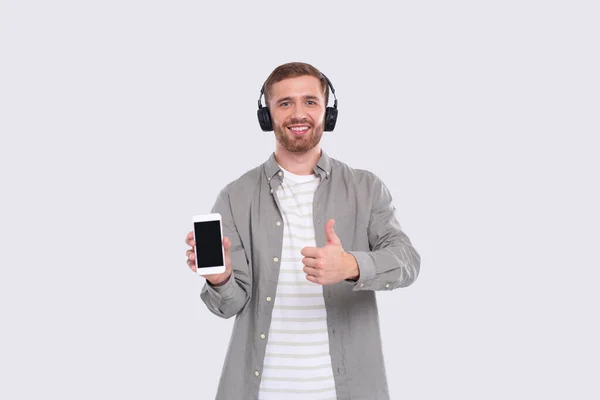 Чоловік слухає музику з телефону, показуючи пристрій і великий палець вгору. Чоловік тримає телефон. Ізольовані — стокове фото