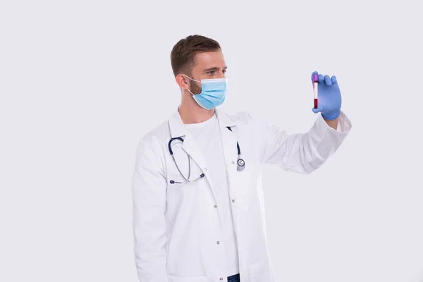 Een man met een bloedbuisanalyse met een medisch masker en handschoenen. Dokter onderzoekt bloedtesten. Wetenschap, medisch concept. geïsoleerd. — Stockfoto