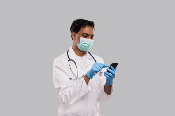 Doutor conversando no telefone vestindo máscara médica e luvas. indiano homem médico com telefone isolado — Fotografia de Stock