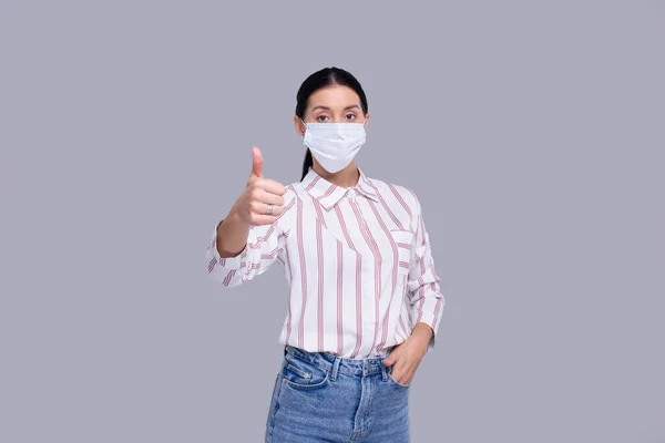 Девушка в медицинской маске, показывающая, что большой палец изолирован. Посмотрите на женщину в офисе в медицинской маске. Здоровье, медицина, изоляция — стоковое фото