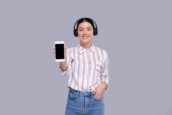 Menina mostrando telefone usando fones de ouvido de pé isolado. Conceito Commecial, Compras, Anúncio — Fotografia de Stock