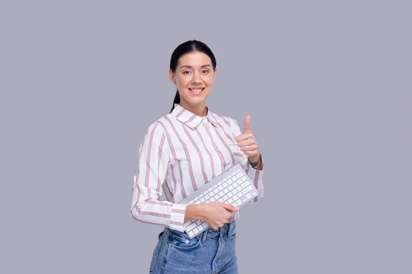 Trabajadora de oficina sosteniendo el teclado en las manos levantando el pulgar. Chica aislada. Concepto de oficina Imagen de archivo