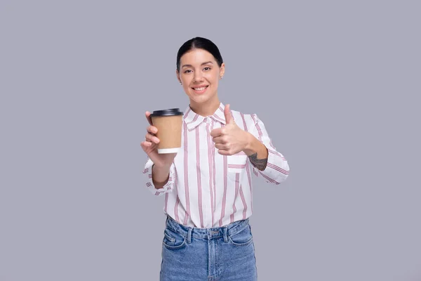 Chica sosteniendo café Take Away Copa Mostrando Pulgar hacia arriba. Chica con para ir taza de café en manos aisladas Imágenes de stock libres de derechos
