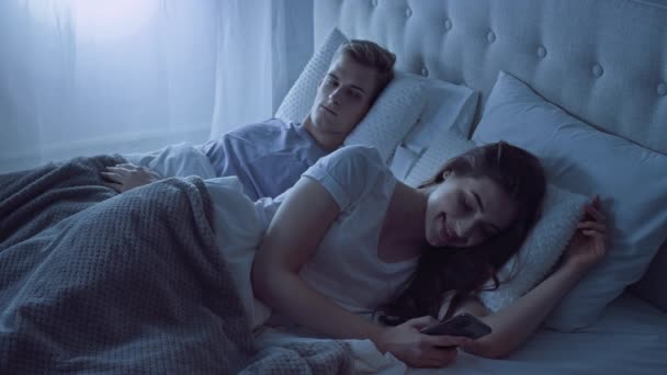 夫妇躺在床上用手机 男人忌妒 在床上过夜的夫妻 — 图库视频影像