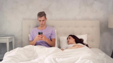 Kız Uyurken Adam Telefonda Sohbet Ediyor. Yatakta Telefonu Kullanan Adam. Kız yatakta uyuyor..