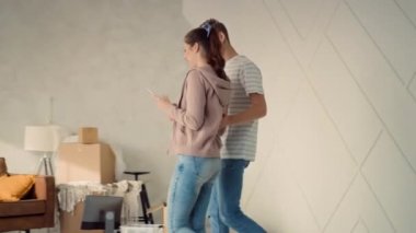 Yeni Evde Tablet Kullanarak Koltukta Oturan Genç Çift. Çift yeni evi tartışıyor. Mutlu Çift Evde Tablet İzliyor.