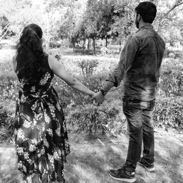 Indian couple posing for maternity baby shoot. The couple is posing in a lawn with green grass and the woman is falunting her baby bump in Lodhi Garden in New Delhi, India - Black and White