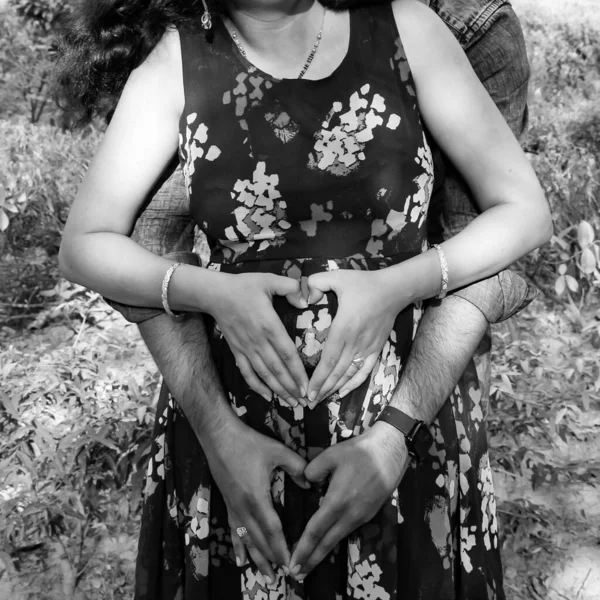 Indian couple posing for maternity baby shoot. The couple is posing in a lawn with green grass and the woman is falunting her baby bump in Lodhi Garden in New Delhi, India - Black and White