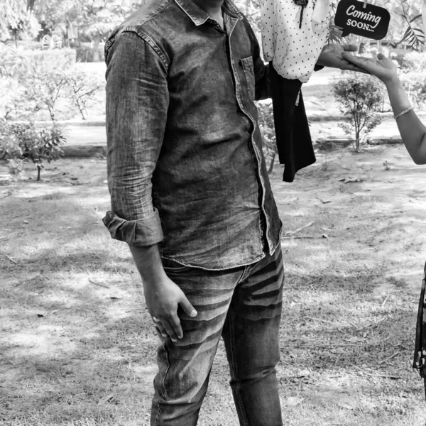 Indian couple posing for maternity baby shoot. The couple is posing in a lawn with green grass and the woman is falunting her baby bump in Lodhi Garden in New Delhi, India - Black and White