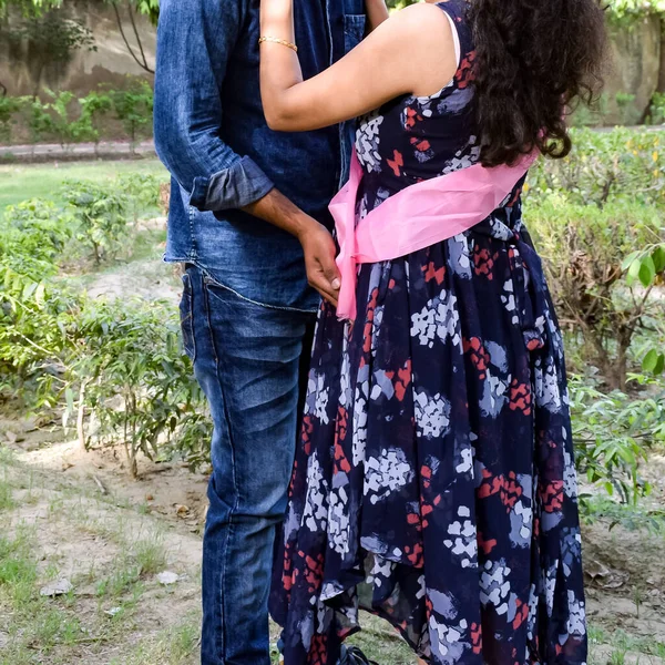 Indian couple posing for maternity baby shoot. The couple is posing in a lawn with green grass and the woman is falunting her baby bump in Lodhi Garden in New Delhi, India