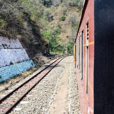 Oyuncak tren dağ yamaçlarında hareket ediyor, güzel bir manzara, bir dağ yamacı, bir vadi yamaçtan tepeye hareket ediyor, yeşil doğal ormanın arasında. Hindistan 'da Kalka' dan Shimla 'ya giden oyuncak tren, Hint treni.