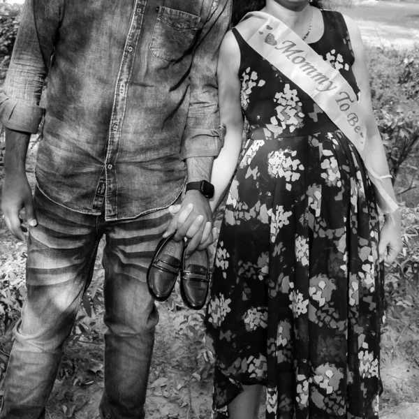 Indian couple posing for maternity baby shoot. The couple is posing in a lawn with green grass and the woman is falunting her baby bump in Lodhi Garden in New Delhi, India - Black and White