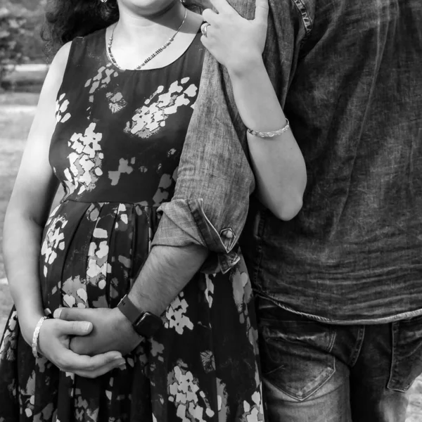 Indian couple posing for maternity baby shoot. The couple is posing in a lawn with green grass and the woman is falunting her baby bump in Lodhi Garden in New Delhi, India - Black and White