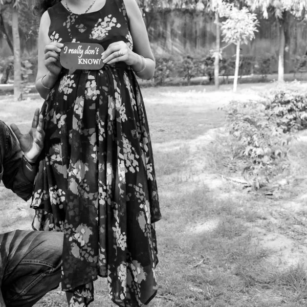 Indian couple posing for maternity baby shoot. The couple is posing in a lawn with green grass and the woman is falunting her baby bump in Lodhi Garden in New Delhi, India - Black and White