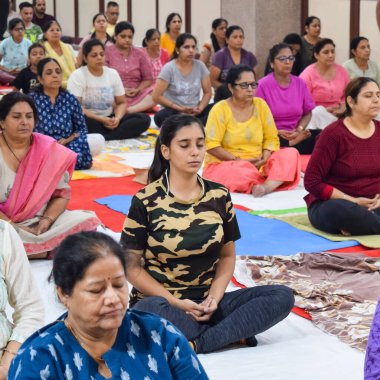 New Delhi, India, June 19 2022 -Group Yoga exercise session for people of different age groups in Balaji Temple, Vivek Vihar, International Yoga Day, Big group of adults attending yoga class in temple