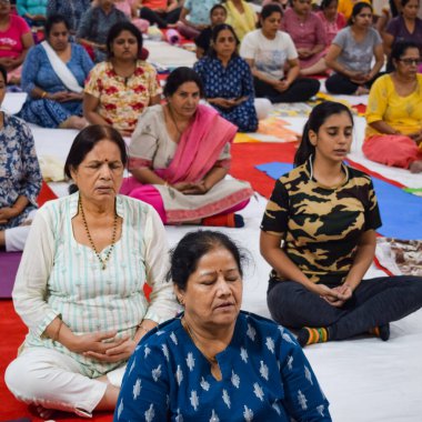 New Delhi, India, June 19 2022 -Group Yoga exercise session for people of different age groups in Balaji Temple, Vivek Vihar, International Yoga Day, Big group of adults attending yoga class in temple