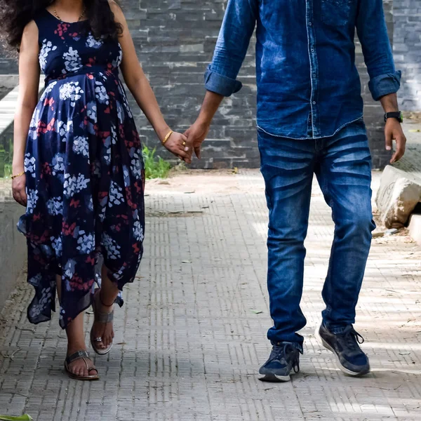 Indian couple posing for maternity baby shoot. The couple is posing in a lawn with green grass and the woman is falunting her baby bump in Lodhi Garden in New Delhi, India