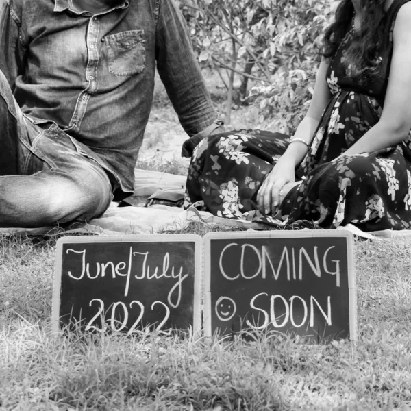 Indian couple posing for maternity baby shoot. The couple is posing in a lawn with green grass and the woman is falunting her baby bump in Lodhi Garden in New Delhi, India - Black and White