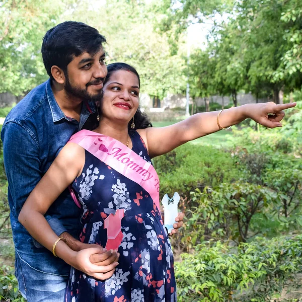 Indian couple posing for maternity baby shoot. The couple is posing in a lawn with green grass and the woman is falunting her baby bump in Lodhi Garden in New Delhi, India