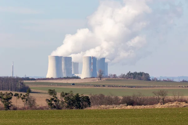 Nuclear power plant - four towers of a nuclear power plant from which steam is smoking in the background blue sky and in the foreground a field.