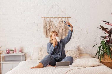 Pijamalı, yatakta dizüstü bilgisayarla çalışan, telefonda konuşan güzel bir genç kadın. İnternetten alışveriş
