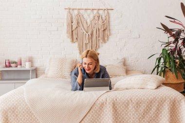 Pijamalı, yatakta dizüstü bilgisayarla çalışan, telefonda konuşan güzel bir genç kadın. İnternetten alışveriş