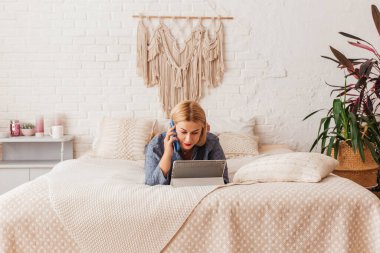 Pijamalı, yatakta dizüstü bilgisayarla çalışan, telefonda konuşan güzel bir genç kadın. İnternetten alışveriş