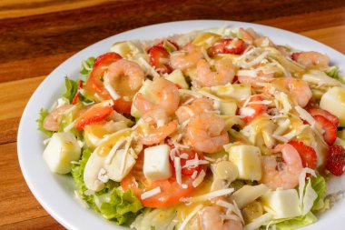 Tahta masanın üzerinde beyaz tabakta karides ve peynir salatası..