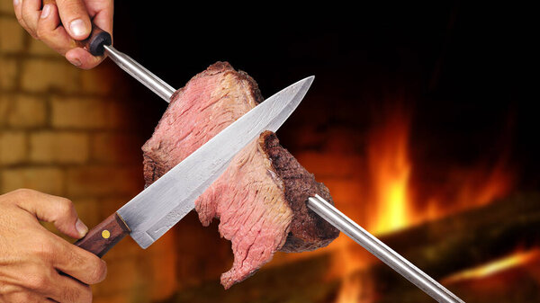Picanha, Brazilian barbecue roasted over hot coals. Knife cutting a piece of meat on a skewer.