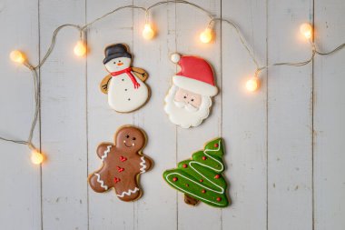 Beyaz ahşap arka planda Noel kurabiyeleri ve ışıklar.