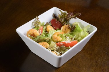 Tahta masada beyaz kasede karidesli yeşil salata..