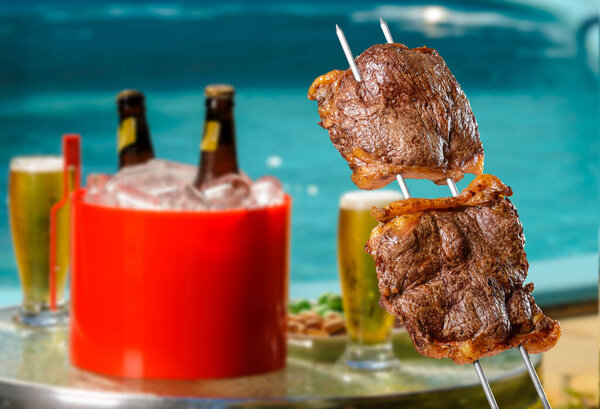 Brazilian barbecue picanha on skewers with blurred beers and pool in the background. — Stock Image Brazilian Barbecue Picanha Skewers Blurred Beers Pool Background Stock Picture