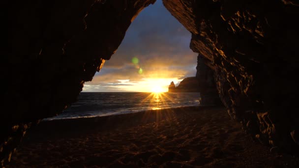 Kilátás a kőbarlangból a naplementére, a tengerre és a strandra, a barlang vulkáni szikláit a meleg lenyugvó nap világítja meg. vulkáni bazalt, mint Izlandon. Szépség világ, természet és a szabadban utazás koncepció