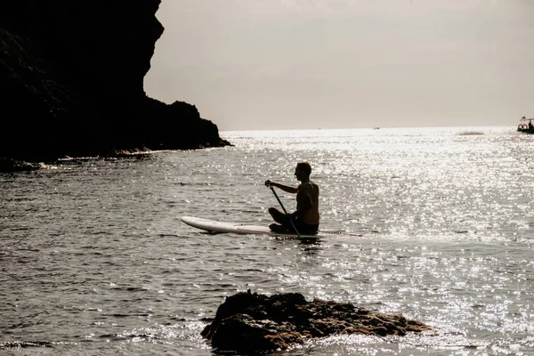 Side view foto of a man swiming and relaxing on the sup board. Sportive man in the sea on the Stand Up Paddle Board SUP. The concept of an active and healthy life in harmony with nature
