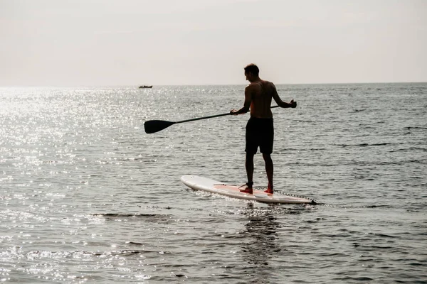 Side view foto of a man swiming and relaxing on the sup board. Sportive man in the sea on the Stand Up Paddle Board SUP. The concept of an active and healthy life in harmony with nature