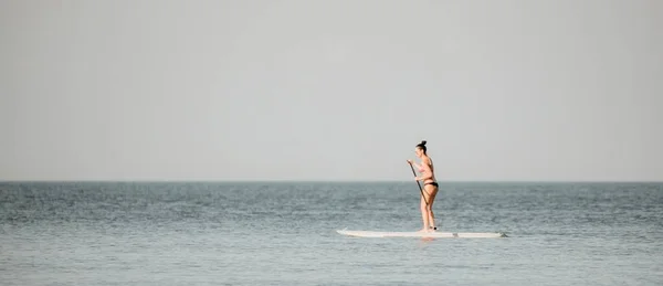 Silhouette of woman standing, surfing on SUP board, confident paddling through water surface. Idyllic sunset or sunrise. Sports active lifestyle at sea or river.