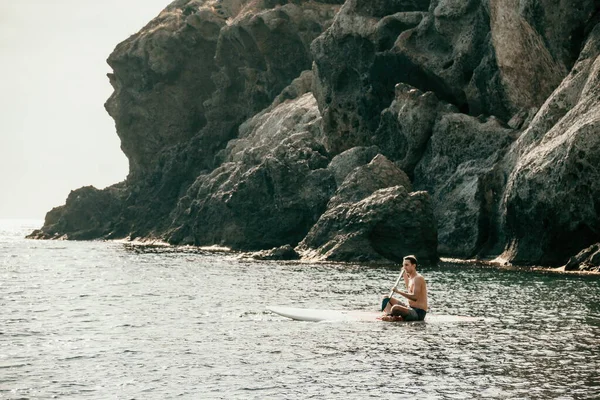 Side view foto of a man swiming and relaxing on the sup board. Sportive man in the sea on the Stand Up Paddle Board SUP. The concept of an active and healthy life in harmony with nature